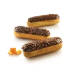 Three chocolate-glazed eclairs decorated with chopped nuts and orange peel