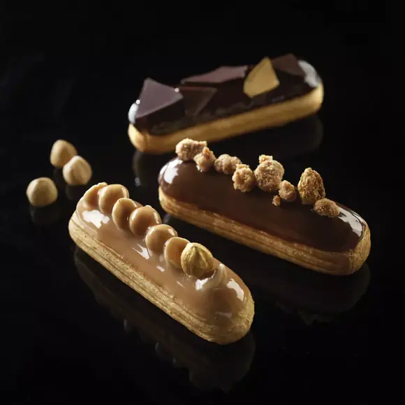 Three glazed chocolate and hazelnut éclairs displayed on a reflective black background