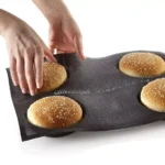 Four round sesame buns being removed from a black Silikomart Airplus 12 microperforated mould
