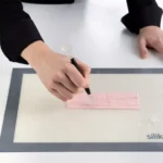Pastry chef using the Silikomart Roll Tool to create decorative lines in pink sugar paste