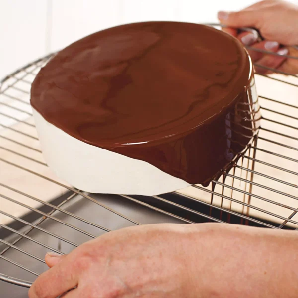 Chocolate glaze being poured over a round cake on a stainless steel cooling grid